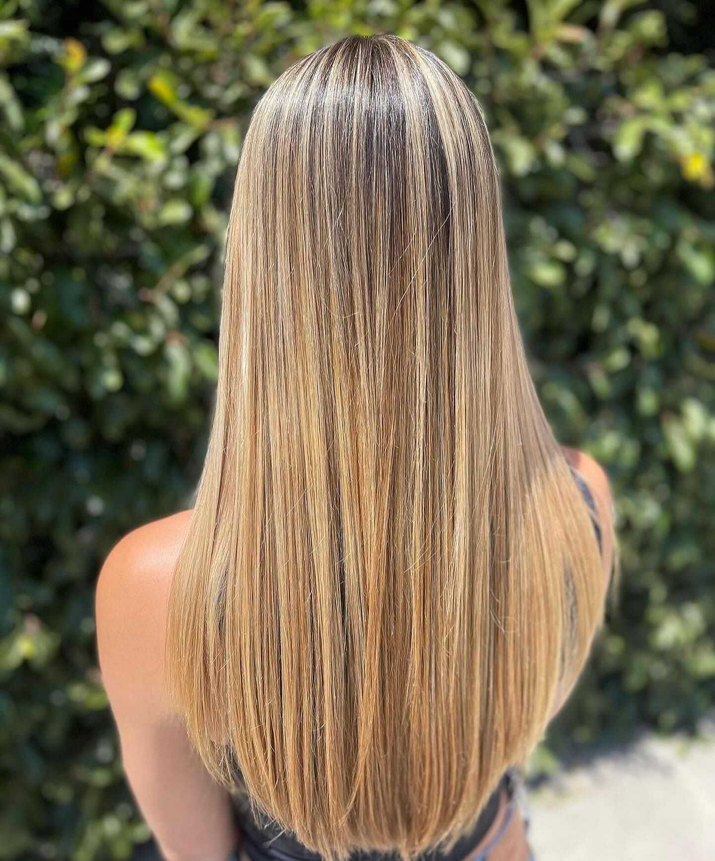 Smooth, straight blonde hair with highlights against a leafy green background.