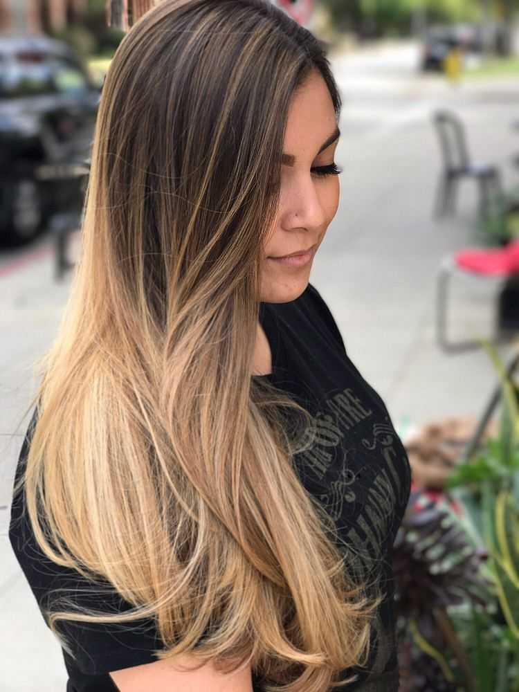 Woman with long, straight brown hair and blonde highlights, standing outdoors.