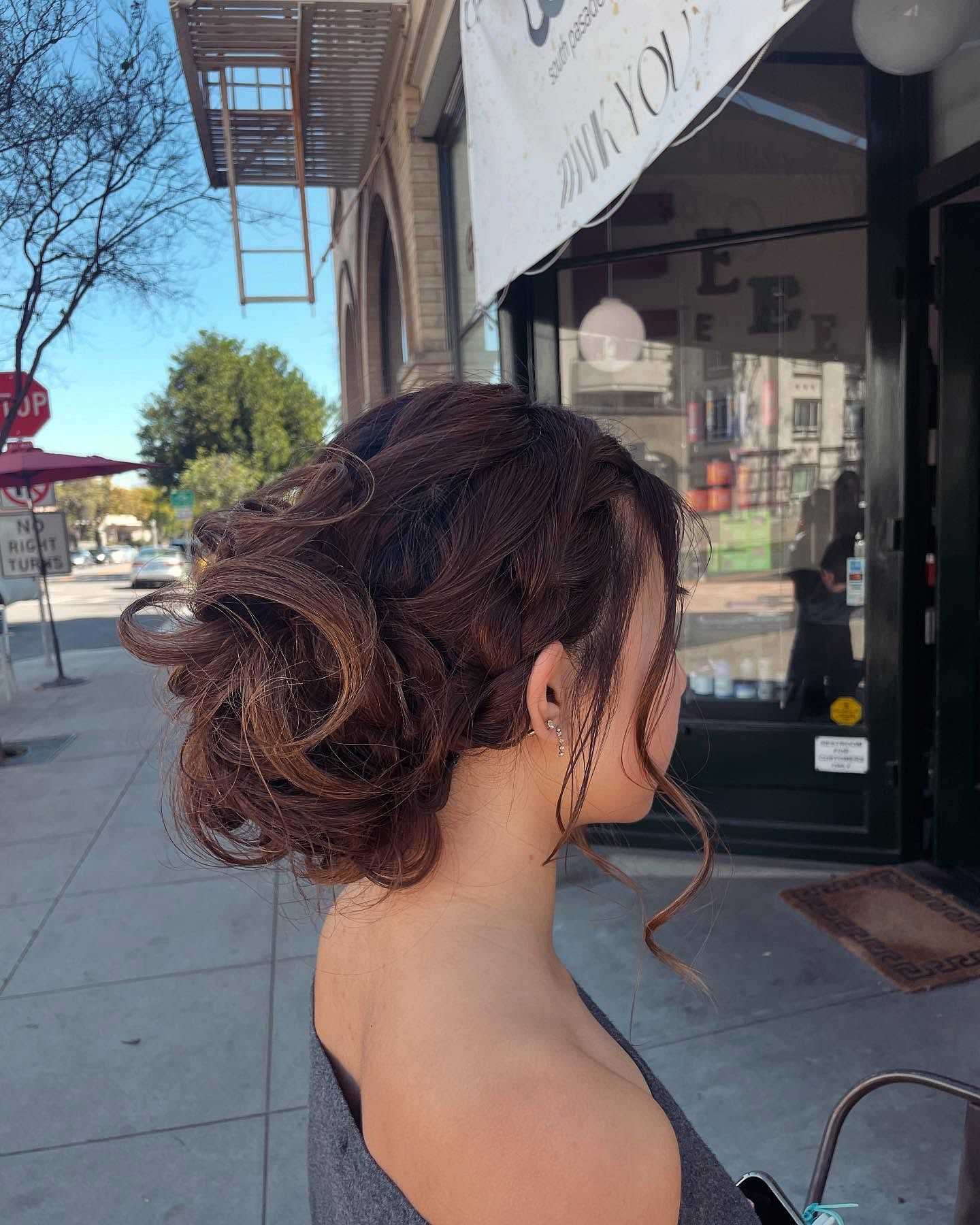 Woman with elegant updo hairstyle standing on a city sidewalk.
